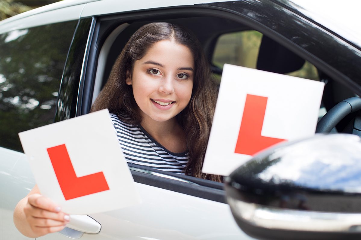 Smiling learner driver holding two L plates out of a car window