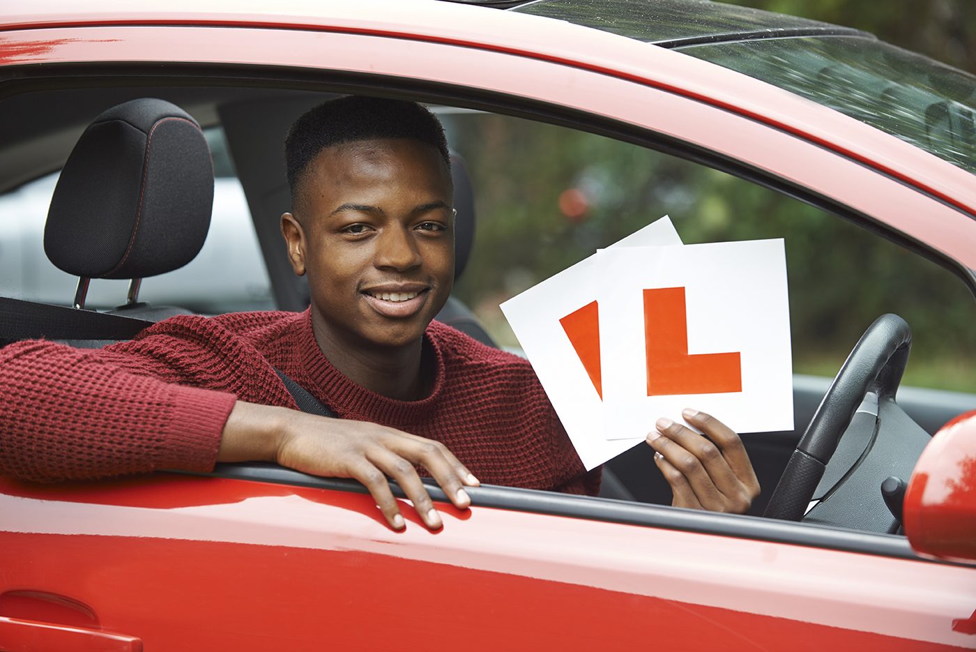 Happy young learner driver holding up L plates from a car